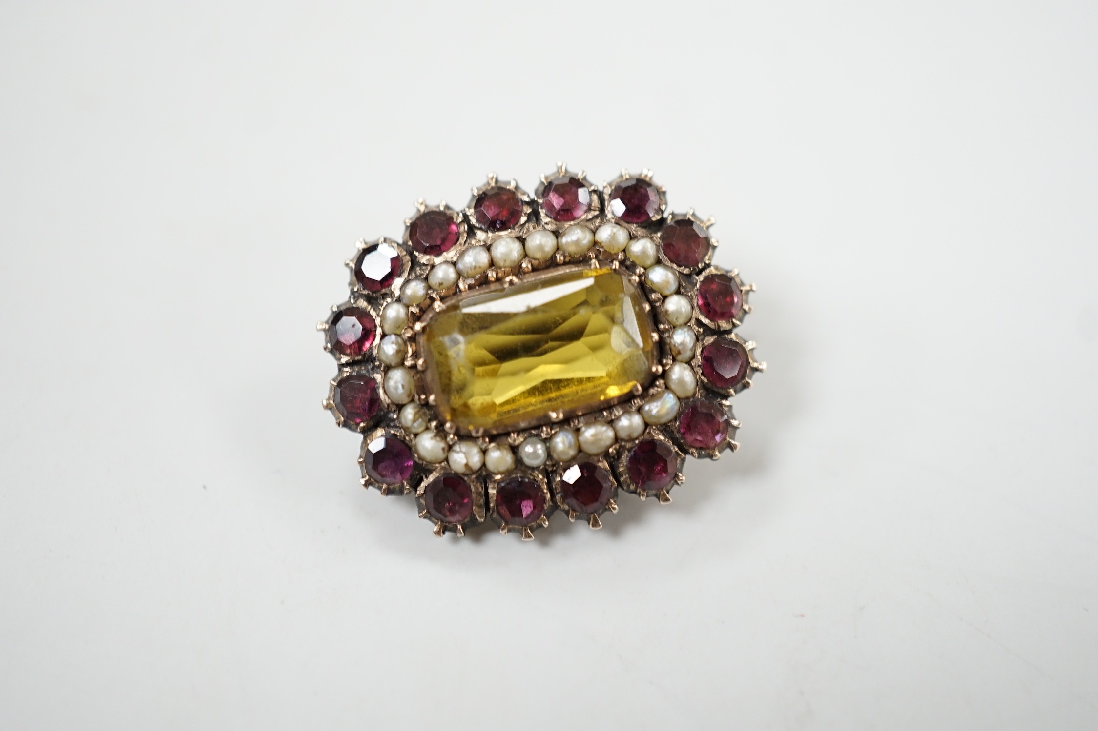 An early 19th century yellow metal, yellow paste, foil backed garnet and split pearl set oval brooch, 24mm.